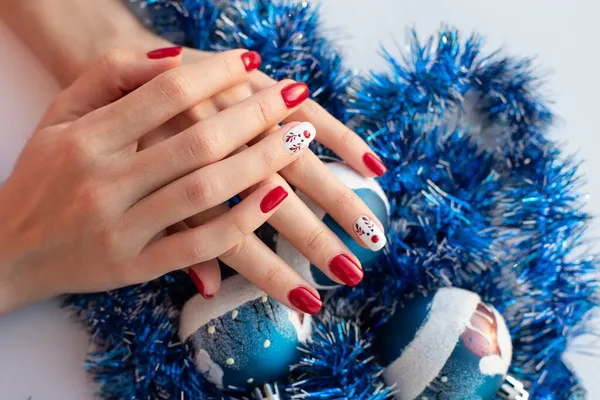 Vörös téli manikűr aranyos szarvas fehér háttér. Egy nő fogja a karácsonyi labdát. Télen és karácsonykor. — Stock Fotó