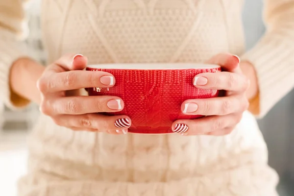Womans hands with french manicure and candy cane pattern on the nails. Woman with beautiful manicure holding big red knitted cup. The concept of cozy Christmas holidays and New Year. — 图库照片