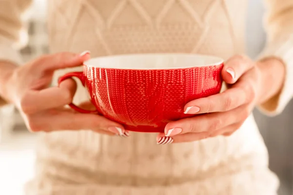 Womans hands with french manicure and candy cane pattern on the nails. Woman with beautiful manicure holding big red knitted cup. The concept of cozy Christmas holidays and New Year. — 图库照片