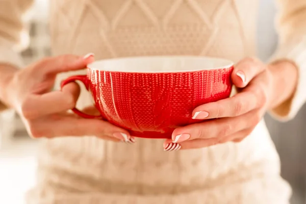 Mãos femininas com manicure francês e padrão de cana-de-açúcar nas unhas. Mulher com bela manicure segurando grande copo de malha vermelha. O conceito de férias de Natal acolhedoras e Ano Novo. — Fotografia de Stock