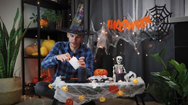 Młody człowiek w kapeluszu czarownicy zapala świece na Halloween Night Party. Dekoracja Halloween — Wideo stockowe