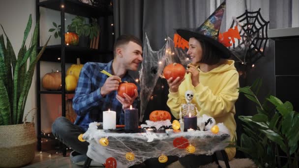 Feliz Dia das Bruxas. Feliz casal alegre amigos pintar abóboras laranja na festa de Halloween — Vídeo de Stock