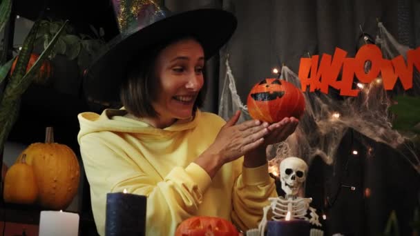 Glad halloween. Spännande ung kvinna i häxa hatt leka med pumpa med målade skrämmande ansikte — Stockvideo