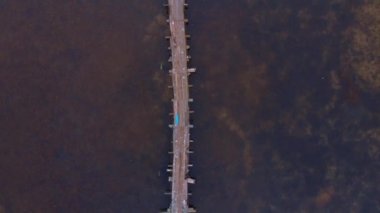 Gün batımında sakin su yüzeyinin üzerindeki boş eski ahşap köprü. Sakin göl