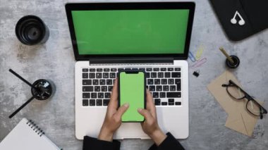 İş kadını çalışma masasında oturuyor, yeşil ekranlı akıllı telefon kullanıyor.