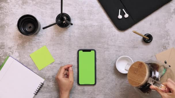 Escritorio con smartphone y material de oficina. Manos vertiendo café negro en la taza en la mesa de trabajo — Vídeo de stock