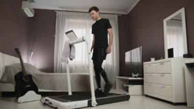 Erkek koşu bandında yürüyor, tabletten ekrana dokunuyor ve çevrimiçi eğitimleri izliyor.