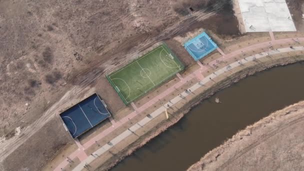 Promenade in de buurt van kleine rivier met sportveld en trainingsvelden, actieve mensen die sport spelen op de speelplaats — Stockvideo
