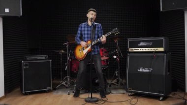 Prova stüdyosundaki gitarist mikrofona rock şarkıları söylüyor.