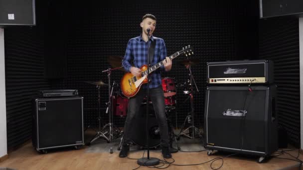 Гитарист в репетиционной студии поет рок-песни для микрофона — стоковое видео