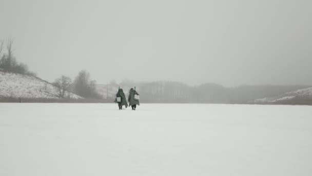 Koncepcja łowienia zimą. Dwóch mężczyzn idzie przez zamarznięte jezioro na zimowe połowy. — Wideo stockowe