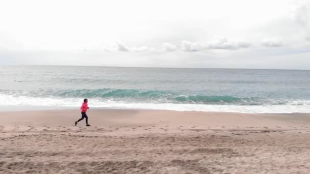 La giovane donna sta facendo jogging sulla spiaggia vuota. Femmina sta correndo attraverso il lato mare al mattino — Video Stock
