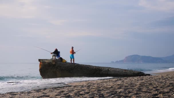 Rybář s prutem sedí na pláži a chytá ryby. Muž se spinning rybaření na pobřeží. — Stock video