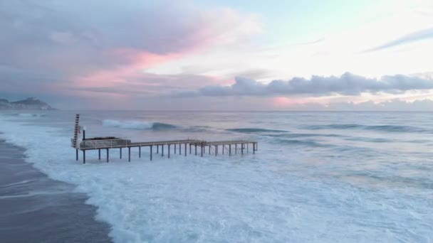 Kraftfulla havsvågor med vitt skum som rullar på stenstrand. Dramatiska rosa moln vid solnedgången — Stockvideo