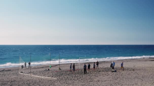 Arkadaşlar plaj voleybolu oynar, kumsalda eğlenir, pas atar ve topu ağın üzerinden fırlatırlar. — Stok video