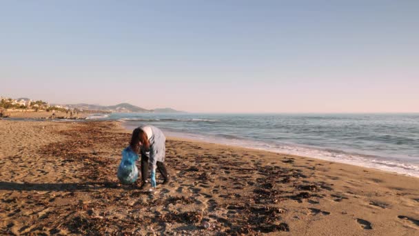 Vrouw verzamelen van plastic afval op het strand, met plastic zak vol met afval — Stockvideo