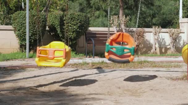 Lege schommelstoelen zwaaiend op kinderspeelplaats. Lege speeltuin — Stockvideo