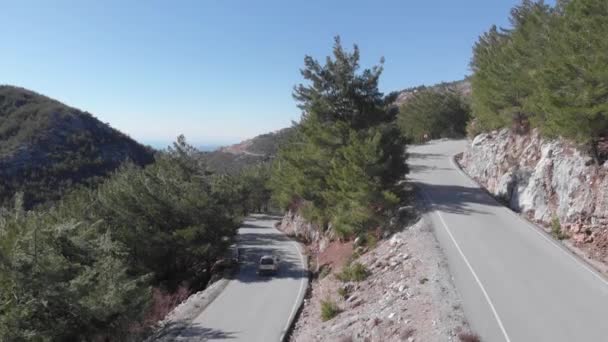 Машина едет вниз с горного перевала. Узкая горная извилистая дорога с зеленым лесом и скалистыми холмами — стоковое видео