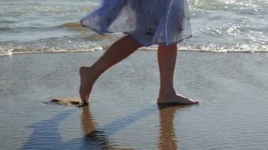 Kumsalda yürüyen bir kadın ayak izi bırakıyor. El sallayan elbiseli çıplak ayaklı kadın deniz kıyısında yürüyor.