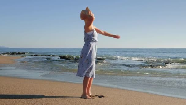 Счастливая улыбающаяся женщина, наслаждающаяся солнечными ваннами и океанским бризом, кружась и веселясь на пляже — стоковое видео