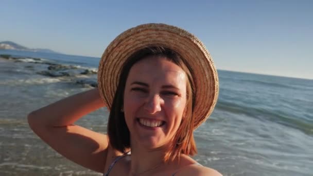 Счастливая улыбчивая девушка, делающая селфи или видео на пляже с селфи в солнечный день — стоковое видео