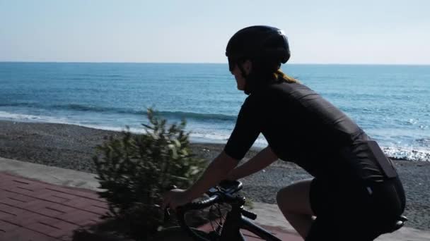 Велосипедистка. Спортивная женщина-велосипедистка катается на велосипеде по набережной у берега моря — стоковое видео
