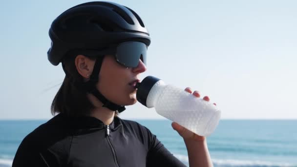 Жінка п'є воду з пляшки після інтенсивного тренування на велосипеді. Велосипедист п'є воду — стокове відео