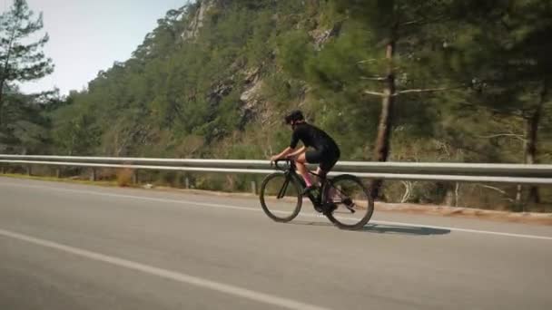 Профессиональное обучение велосипедистов. Женщина в стильной черной велосипедной одежде, шлеме и солнцезащитных очках на велосипеде — стоковое видео