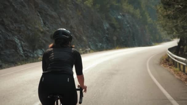 In bicicletta. Ciclista professionista su strada in bicicletta su strada asfaltata vuota tra alberi e montagne — Video Stock