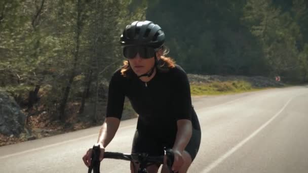 Bisikletçi dağlarda virajlı yolda gidiyor. Gün batımında bisiklet süren atletik formda bir kadın. — Stok video
