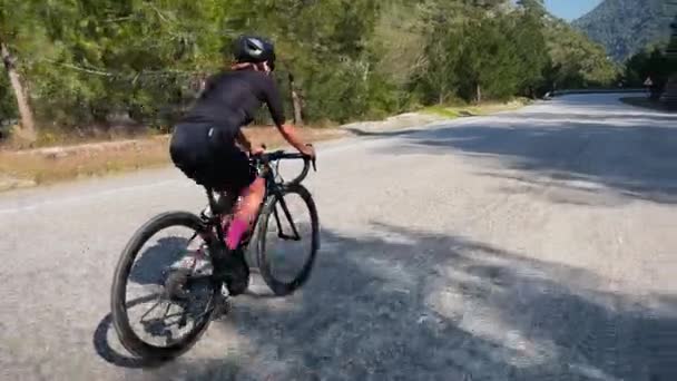 太陽の下で山道を自転車でサイクリング 木の森や山の丘を介してプロの女性サイクリストのロード自転車に乗る サイクリングスポーツのコンセプト 自転車で屋外でのトライアスロントレーニング — ストック動画