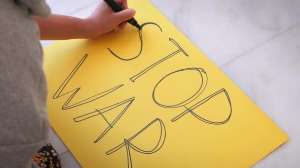 Une femme dessine une bannière avec inscription Stop War sur papier jaune pour soutenir l'Ukraine — Video