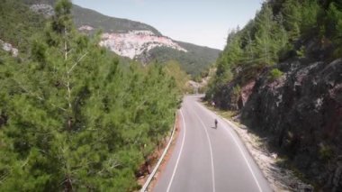 Bisikletçi dağ yolunda bisiklet sürüyor. Güneşli bir günde dağlarda bisiklet süren bir kadın.