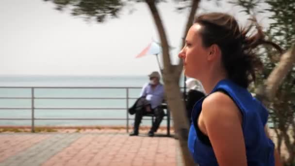 Концепция запуска. Мотивированная женщина бегает по набережной вдоль побережья в солнечный день — стоковое видео