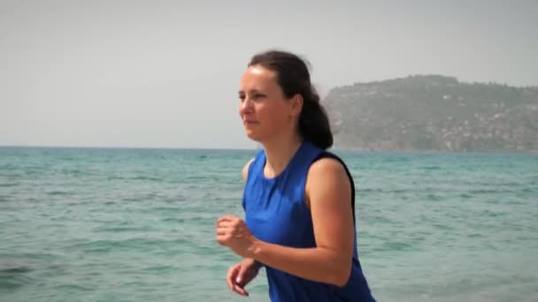 Женщина бегает по пляжу в летний солнечный день. Спортивная бегунья на берегу моря — стоковое видео
