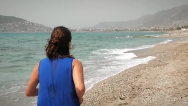 Indietro seguire colpo di femmina che corre sulla spiaggia lungo la riva del mare. Donna joggs all'aperto — Video Stock