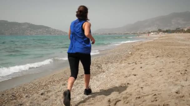 Una donna che corre. Adatta atleta femminile motivata che fa jogging sulla spiaggia vicino al mare — Video Stock