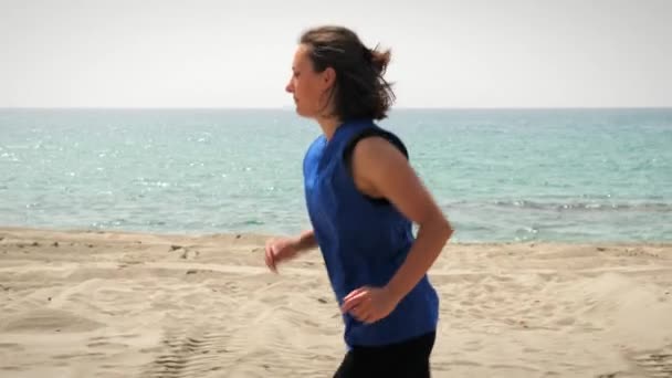 Бег по пляжу с морем на горизонте. Подходящая для бега женщина на песчаном пляже — стоковое видео