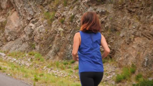 Mujer corriendo al aire libre, empujándose al máximo. Jogging femenino en carretera de montaña — Vídeo de stock