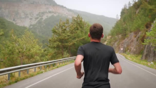 Hombre trotando en la carretera en las montañas, manteniendo un estilo de vida activo deportivo saludable — Vídeo de stock