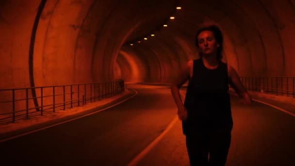Kvinnan springer i tunneln mot kameran. Kvinnliga löpare joggar längs tom tunnel — Stockvideo