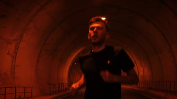 Confident muscular man running along tunnel. Young male athlete jogging outdoors — ストック動画