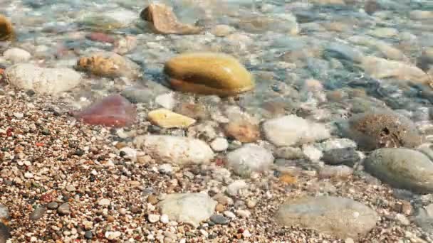 Край воды на галечном морском пляже. Цветные гальки с прозрачными волнами морской воды — стоковое видео