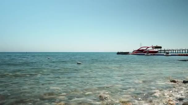Sea pebble beach with moored red yacht near beach. Summer beach vacation — Vídeos de Stock