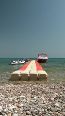 Çakıl taşlı sahilde yüzen plastik duba, demirli jet motorları, dikey video.