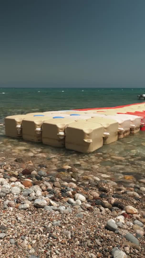 Pebble beach at seashore with pontoon floating on water surface, vertical video — Stock Video