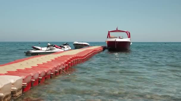 Guijarro en la orilla del mar Mediterráneo con barco de velocidad roja amarrado y motos a reacción — Vídeos de Stock