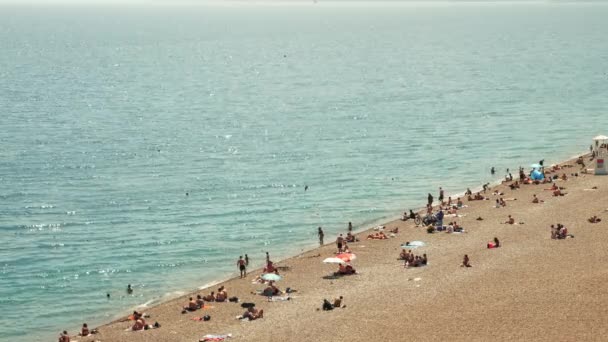 Playa de arena con gente disfrutando del verano. Personas tomando el sol en la playa bajo sombrillas — Vídeo de stock