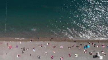 Coastal beach with people lying under umbrellas. Tropical seashore with calm sea