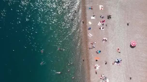 Playa de guijarros con tumbonas y sombrillas. Personas tumbadas en la playa en el caluroso día de verano — Vídeo de stock